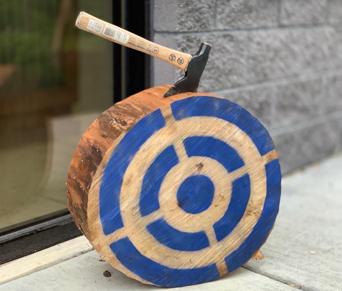 A hatchet stuck on the top edge of a round wooden target